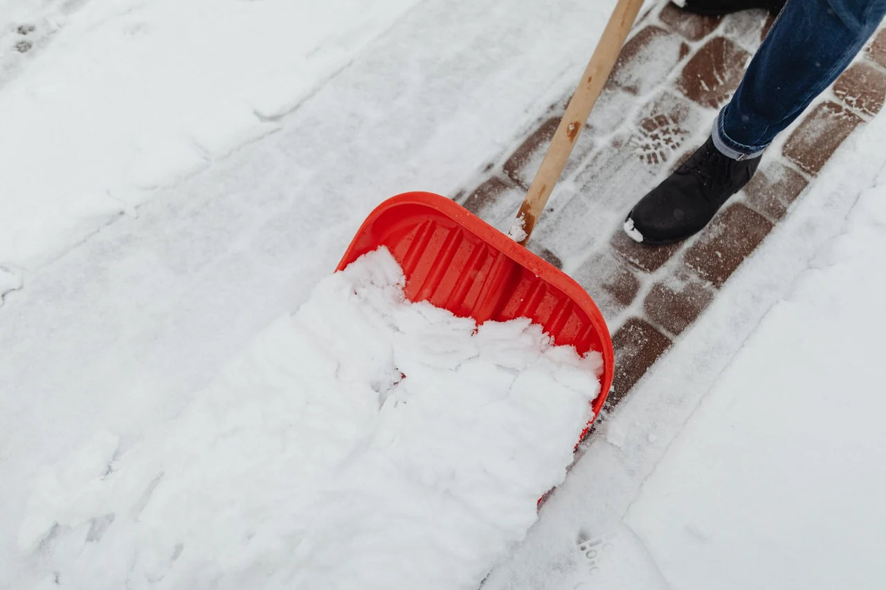 A worker clearing a driveway with a snow shovel after a winter storm